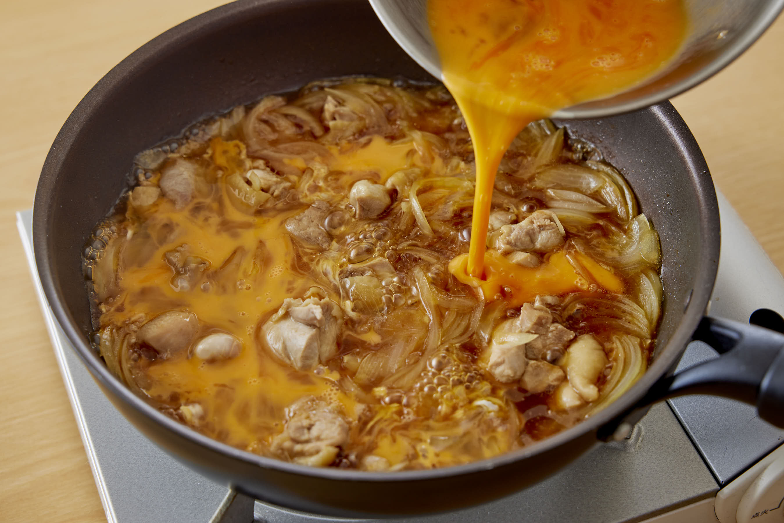 Pouring the beaten eggs in a thin stream across the surface of broth (second time)