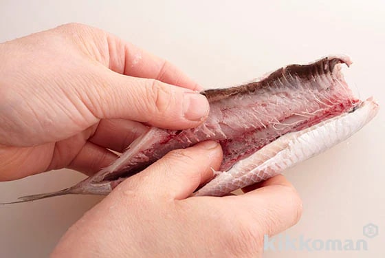 At this point, wrap the innards up in a newspaper, throw these away and rinse the sardine with water and then pat dry to remove excess moisture. Put your thumb inside the cut near to the top of the backbone, then slide this down towards the tail to split open.