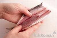 At this point, wrap the innards up in a newspaper, throw these away and rinse the sardine with water and then pat dry to remove excess moisture. Put your thumb inside the cut near to the top of the backbone, then slide this down towards the tail to split open.